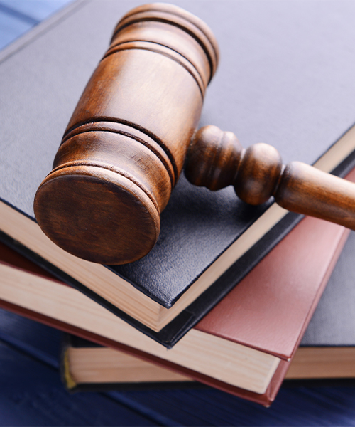 A photograph with a top-down perspective of a gavel on top of three stacked books, placed on a table with a blue tablecloth.